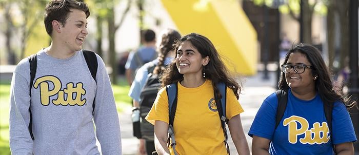 three smiling students walking together on campus on sunny day