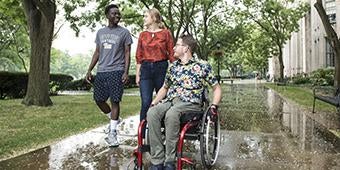 three students, one in a wheelchair, together on Pitt campus